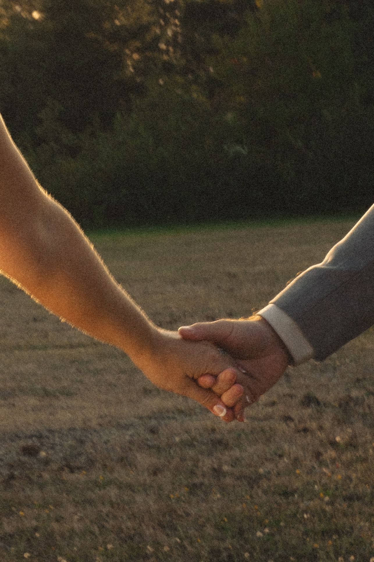Close-up shot of two hands clasped together against a sunset backdrop.