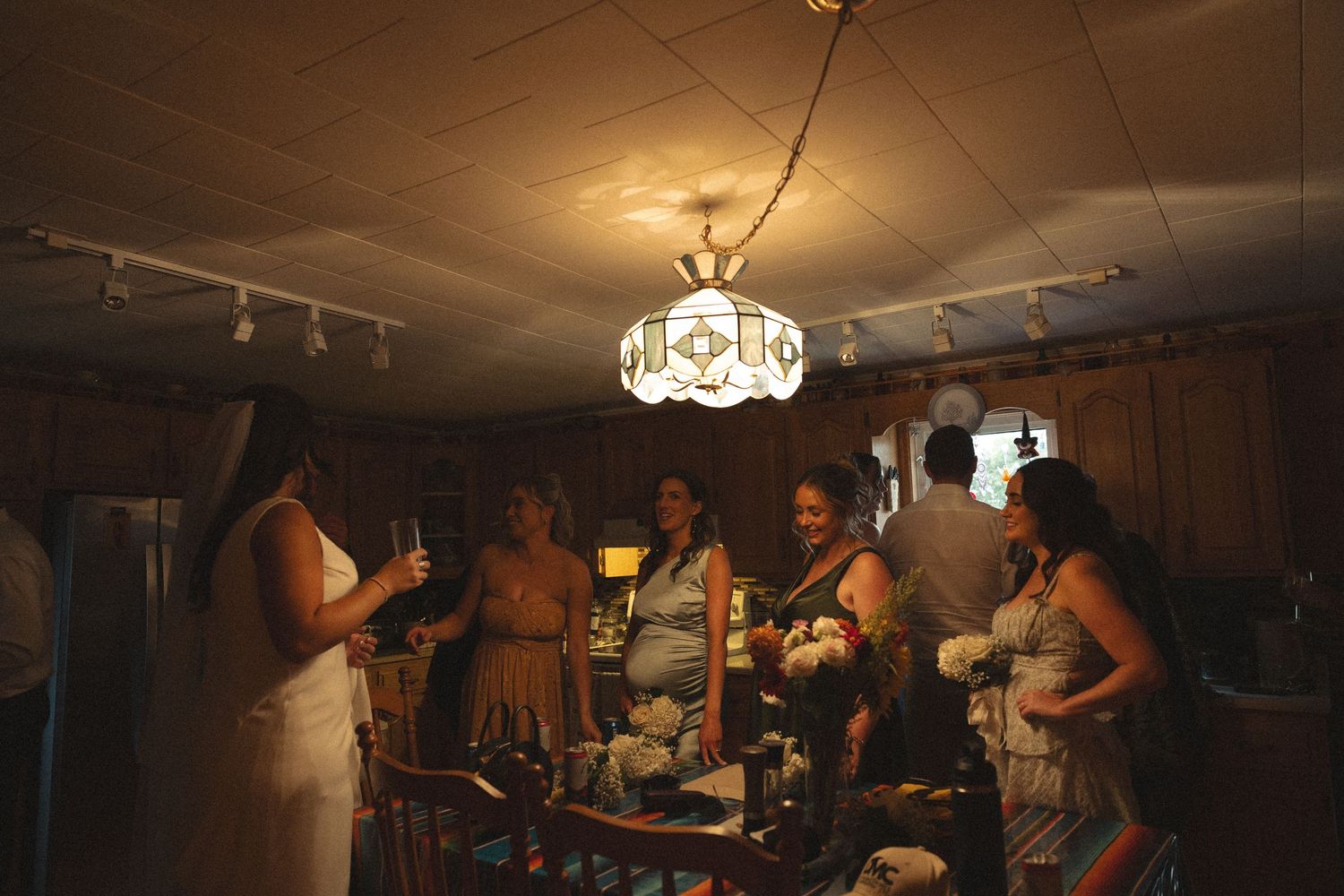 Wedding celebration in a dimly lit indoor space with guests mingling under vintage chandelier lighting.
