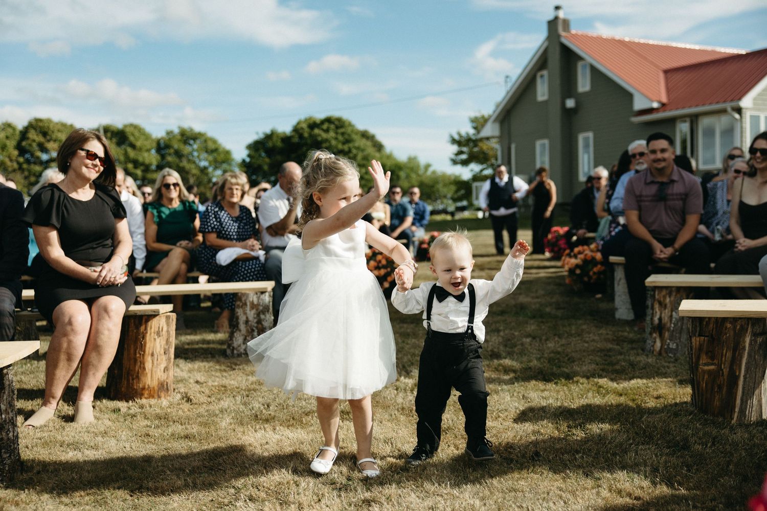 Rustic outdoor wedding celebration with guests seated on hay bales under blue skies.