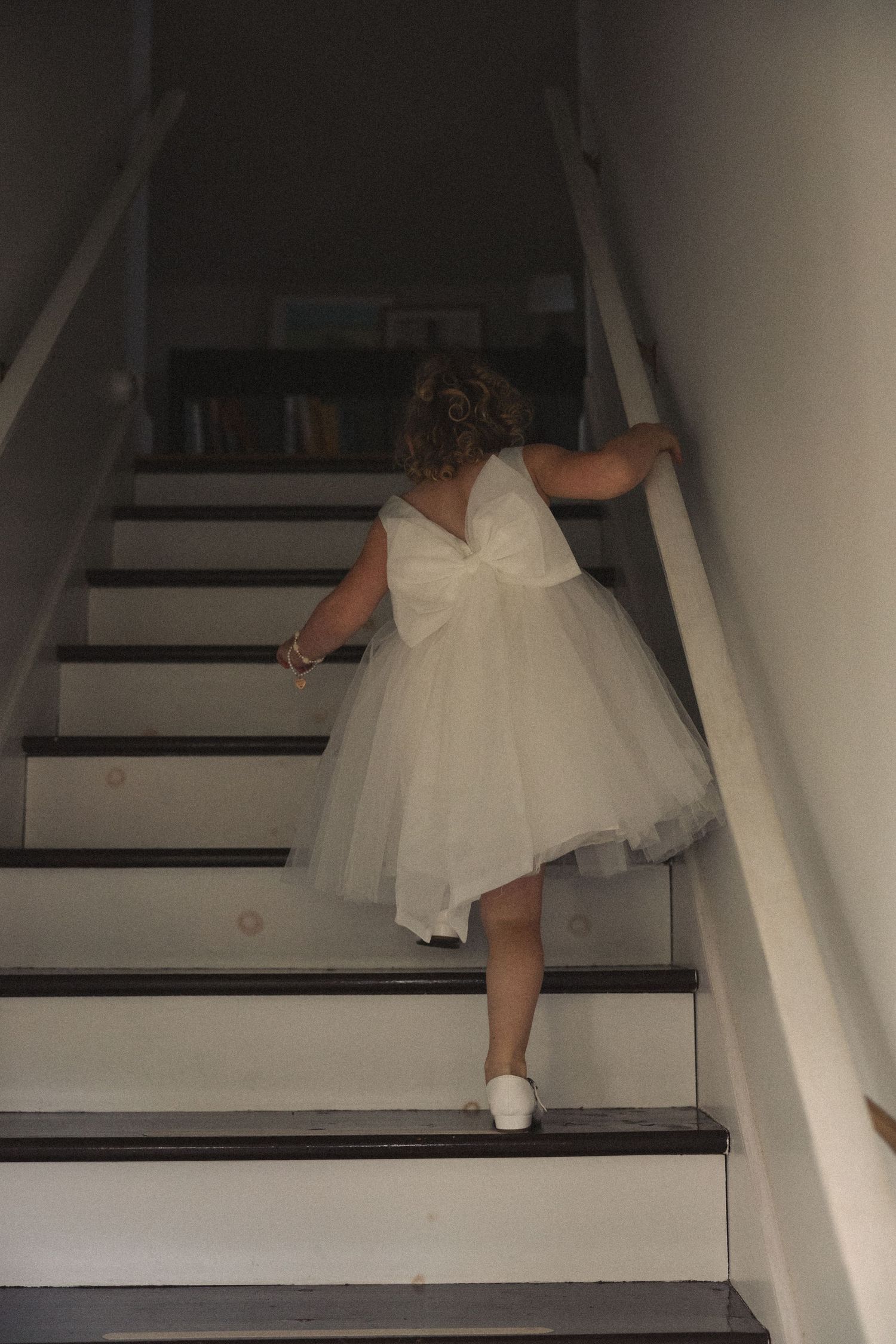 White dress flowing down wooden staircase in dim lighting.