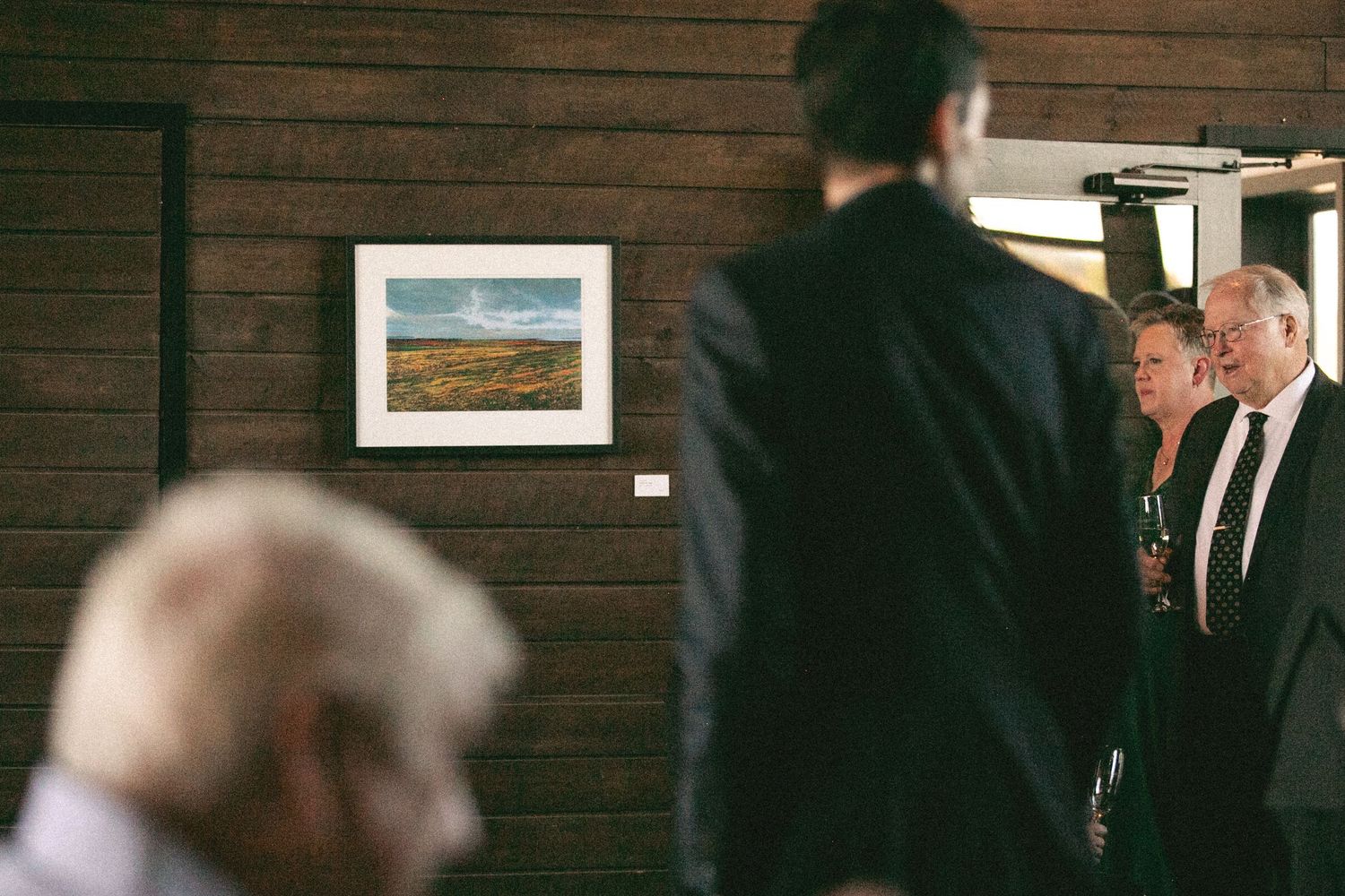 Guests mingling in a wood-paneled room with framed landscape artwork on the wall.