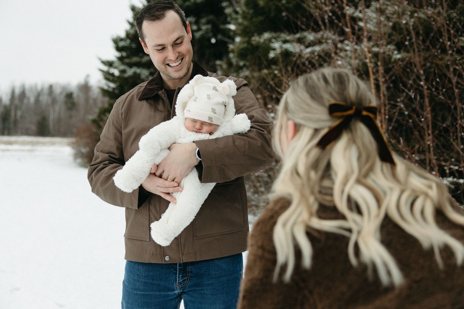 Family portrait in winter setting with baby wearing white snowsuit.