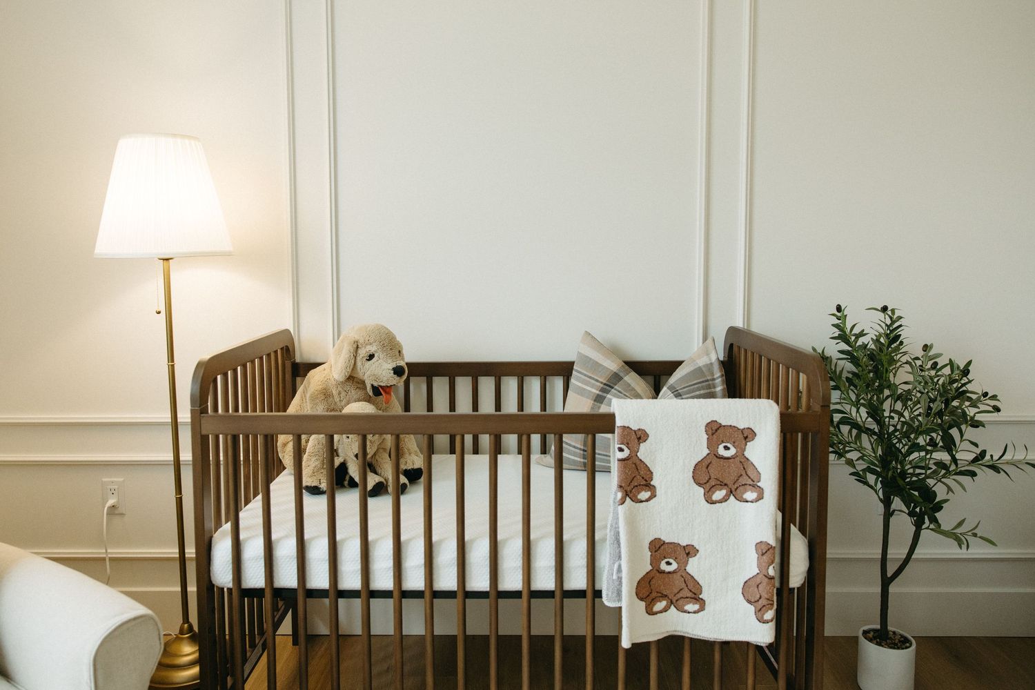 Nursery room with wooden crib, teddy bear decor, and natural light streaming through windows.