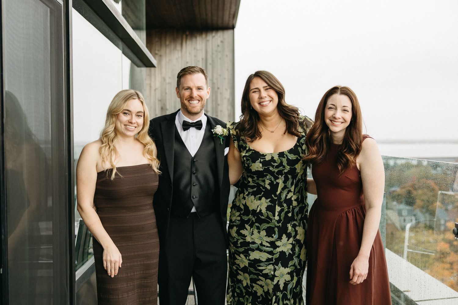 Four people in formal attire stand together on a modern balcony.