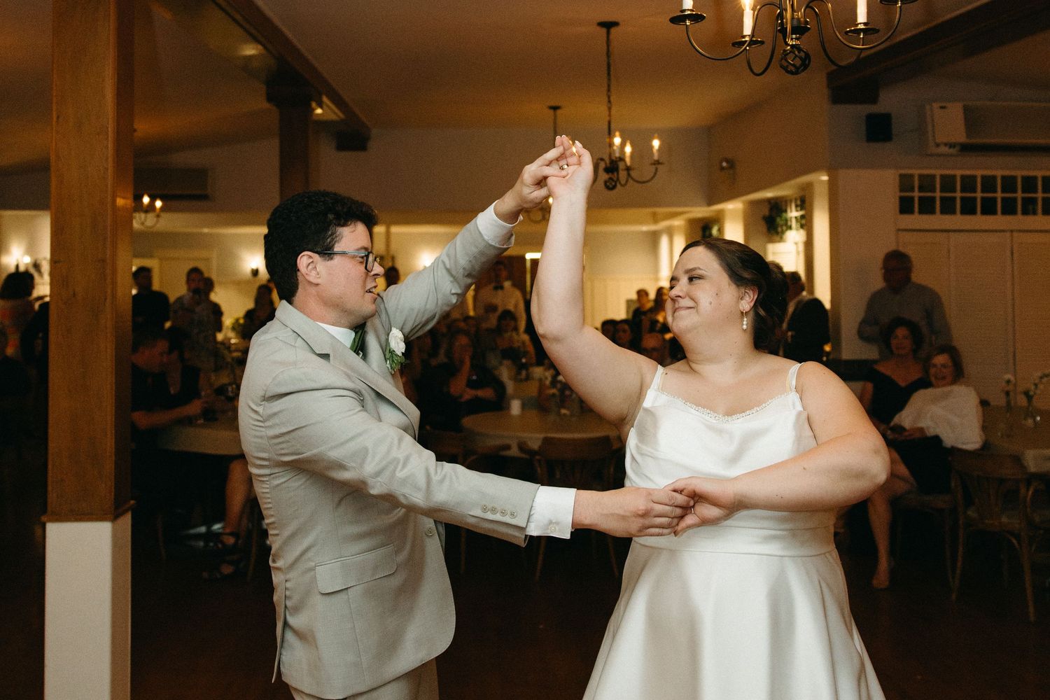 Groom in gray suit twirling bride in white dress on the dance floor at their wedding reception.