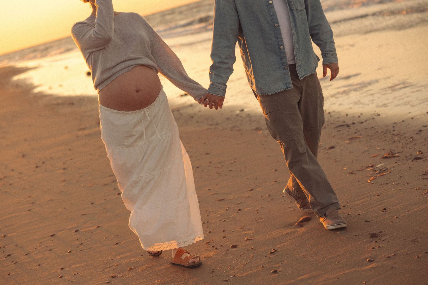 Couple walking hand in hand along beach shore during golden sunset.