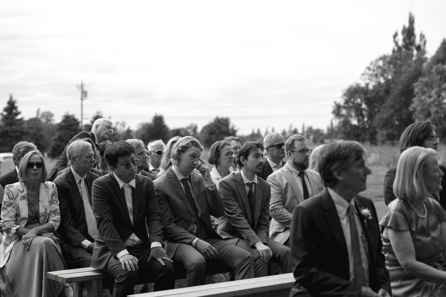 Black and white panoramic shot of wedding guests seated in rows at an outdoor ceremony.