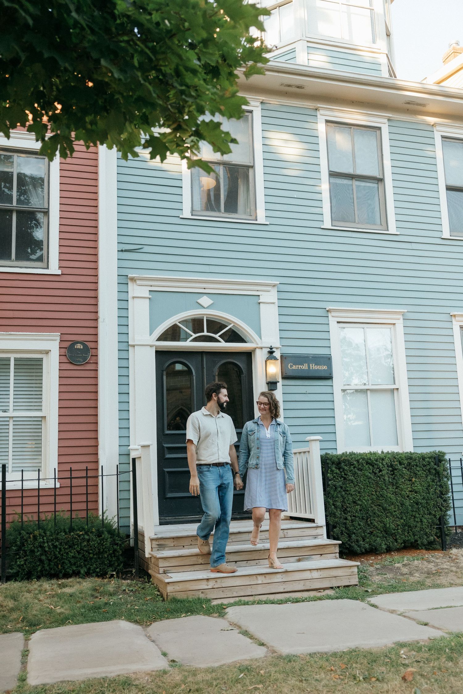 Couple walking along sidewalk past historic pastel-colored townhouses with white trim.