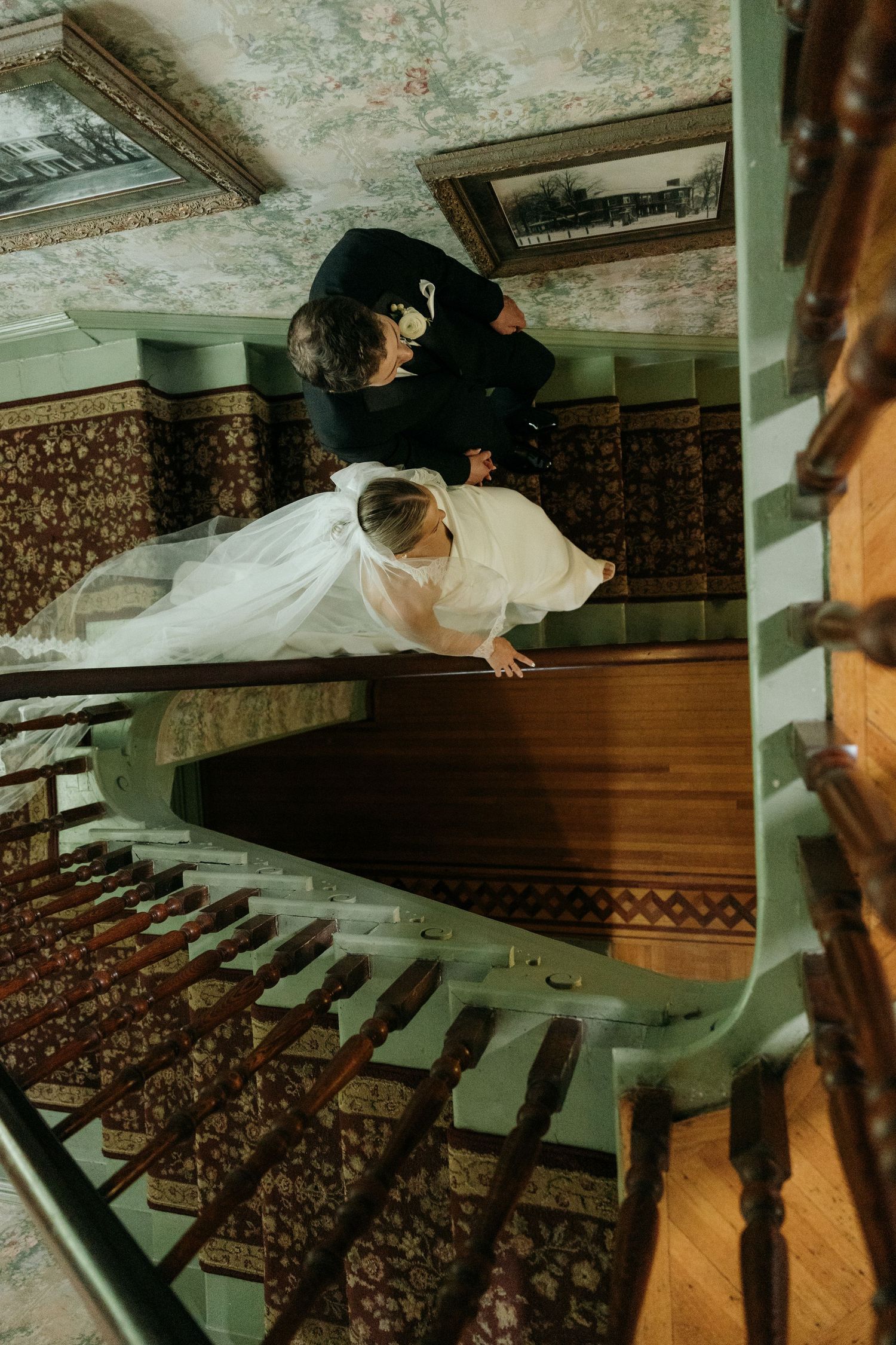 Artistic overhead shot of couple on vintage staircase with ornate carpet and dramatic lighting.