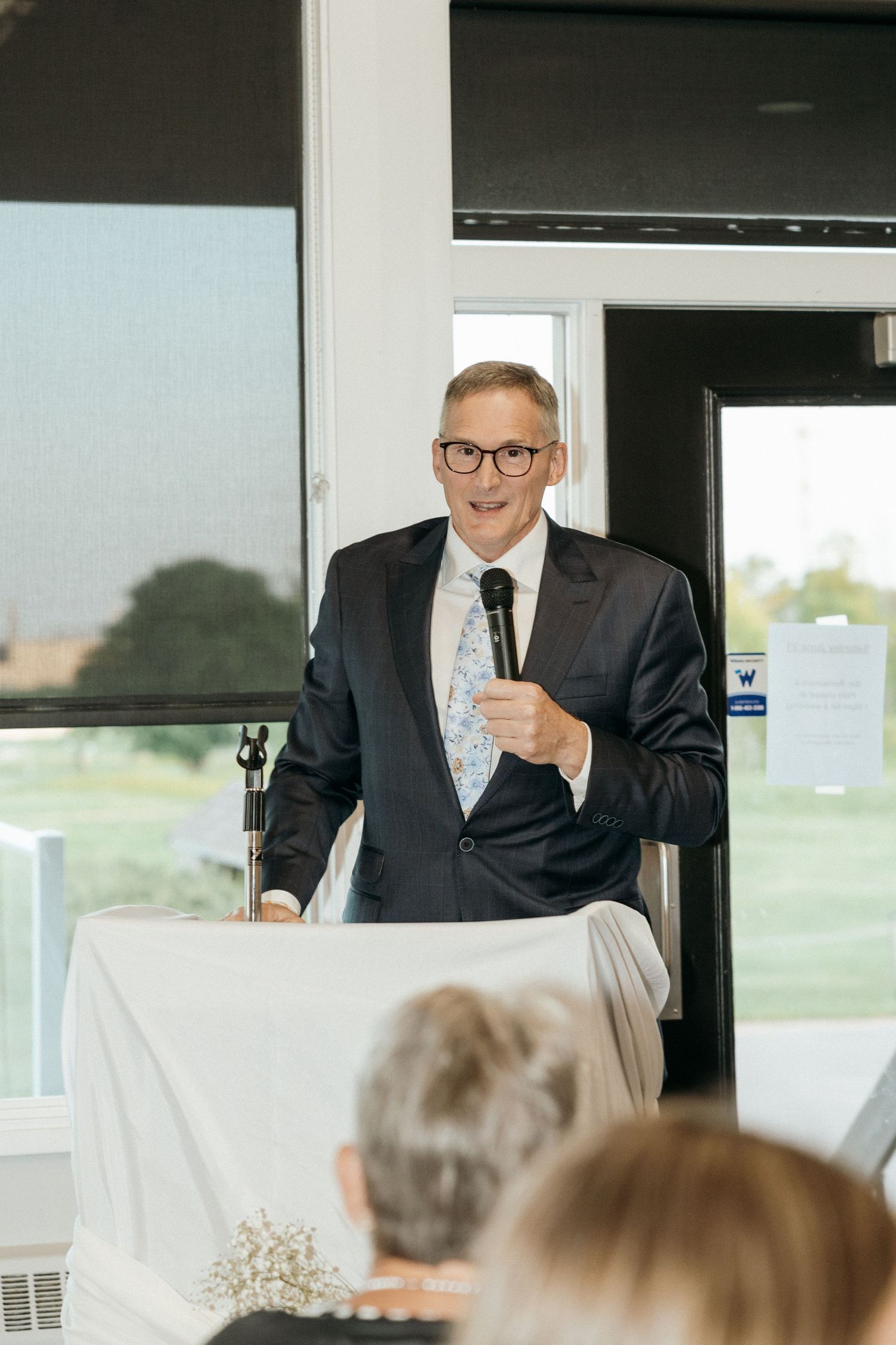 Speaker in suit and glasses gives speech at podium during formal event.