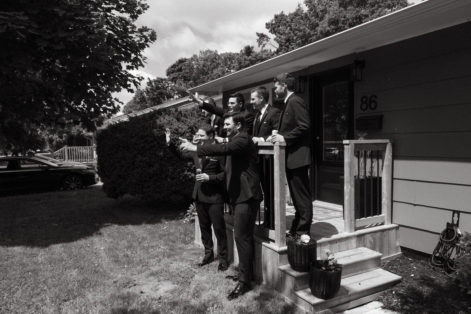Wedding party members in dark suits congregate outside a modern house.