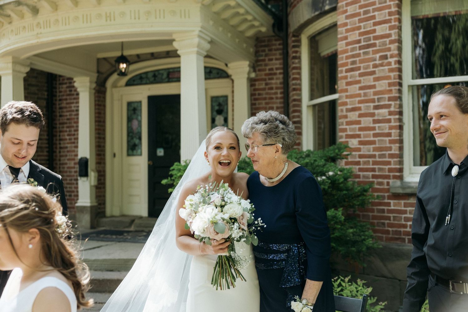 Wedding party gathered under the ornate portico of a historic brick mansion.