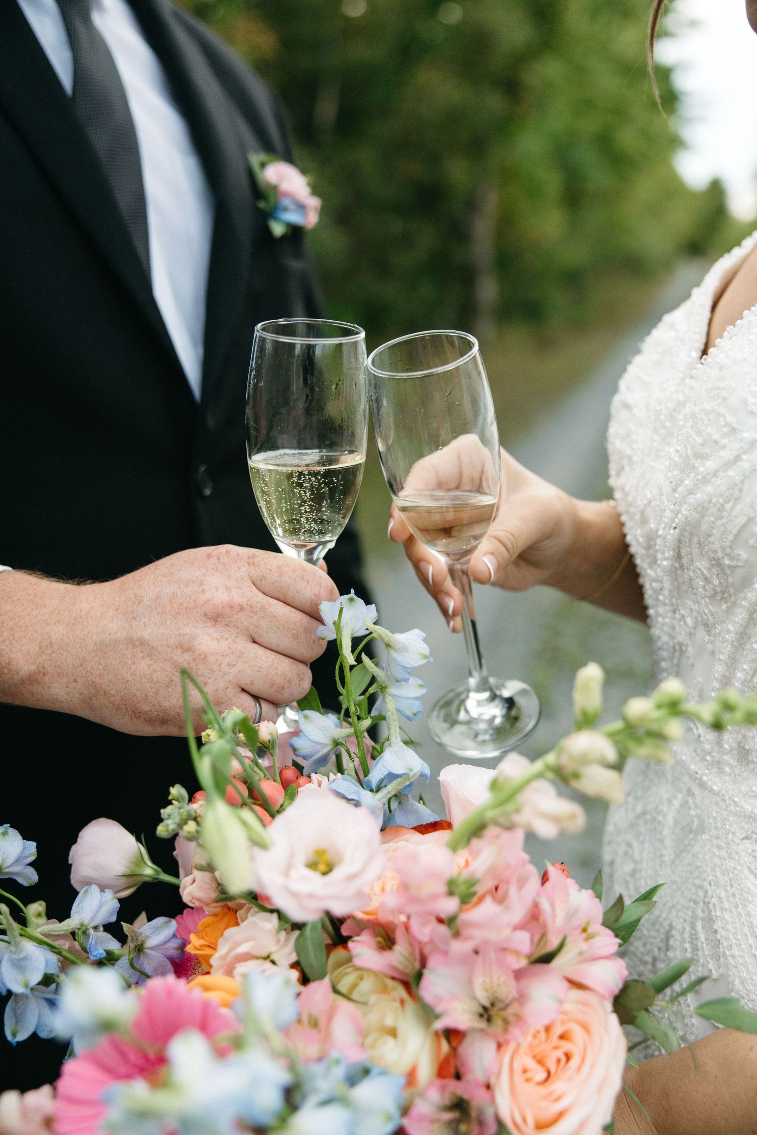 Close-up of champagne toast with colorful wedding bouquet featuring pink roses and blue flowers.