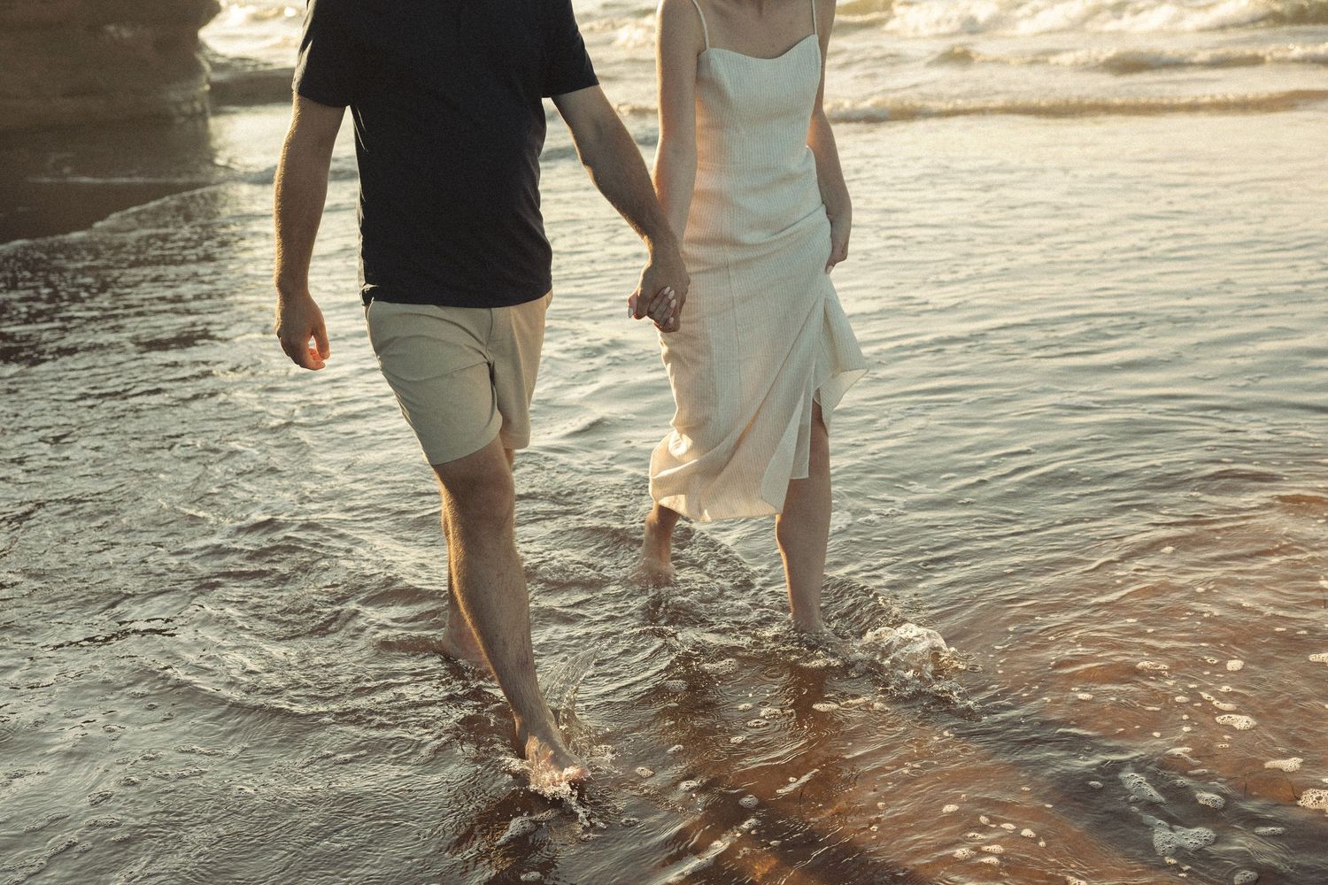 Couple's feet walking together in shallow ocean water at sunset.