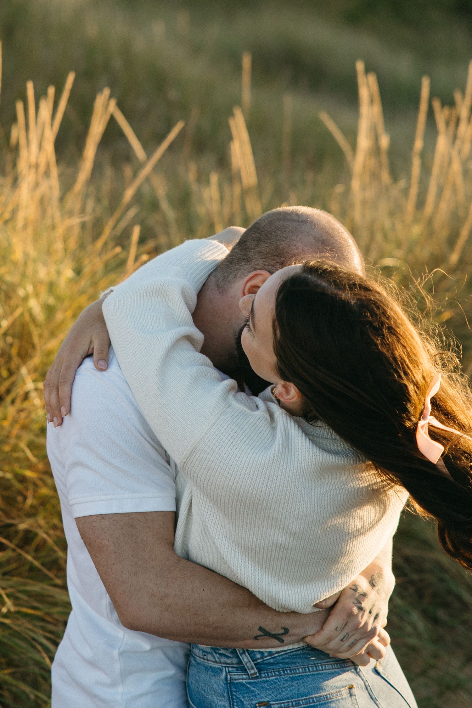 Loving couple embracing in a field of golden grass during sunset.