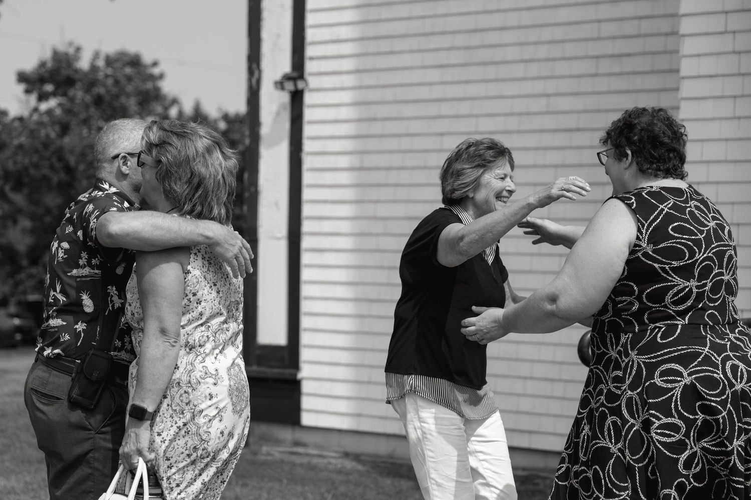 Wedding guests interact outside a white building during reception.