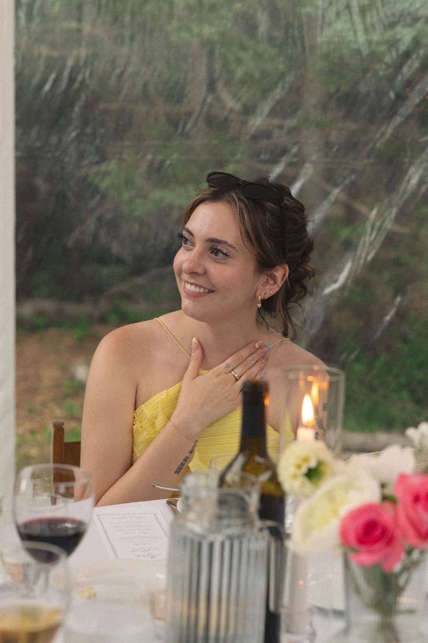 Young woman in yellow dress smiling at wedding reception table with candles and wine.