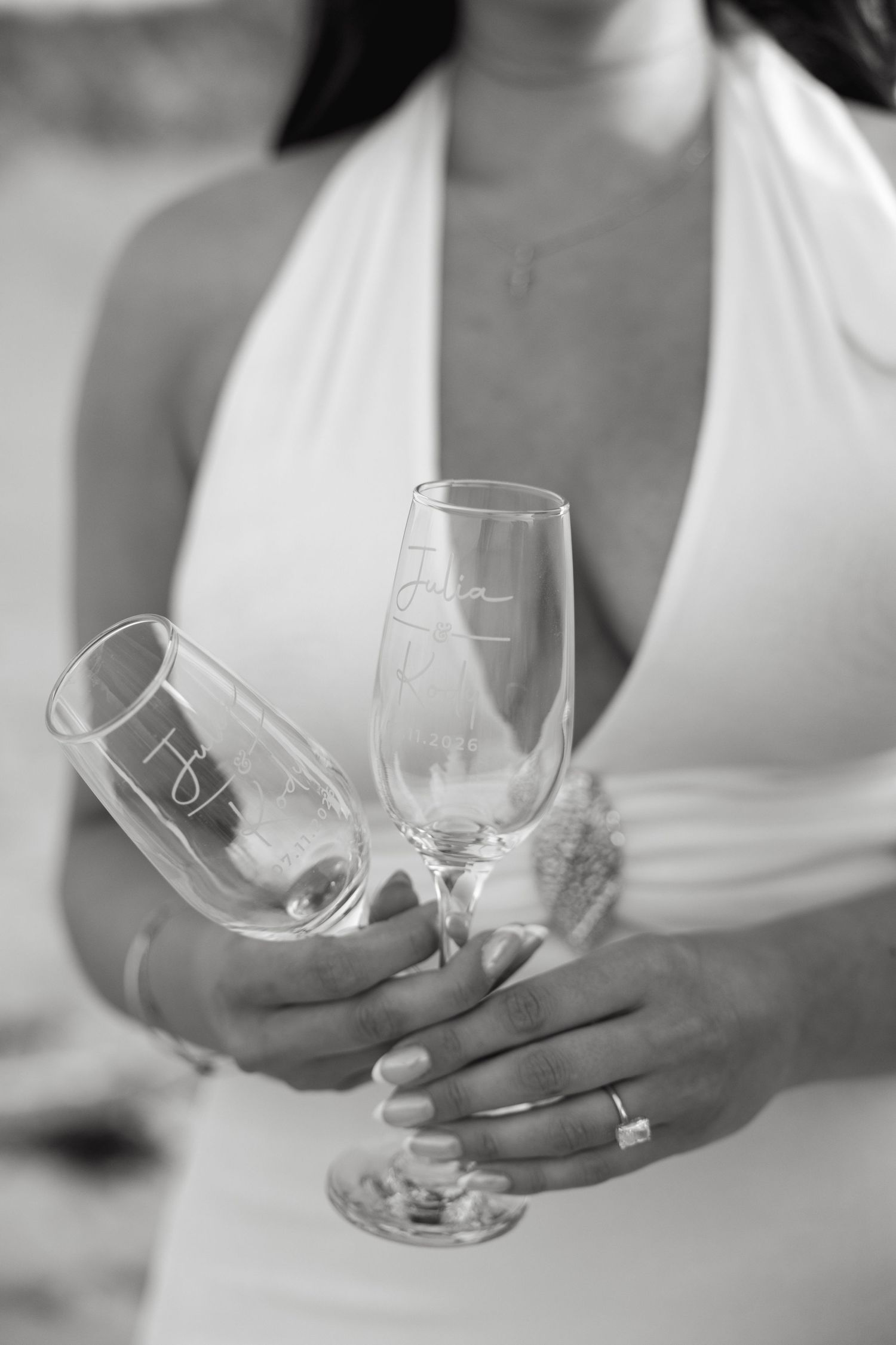 Black and white photo of bride holding two personalized engraved champagne flutes at beach wedding.