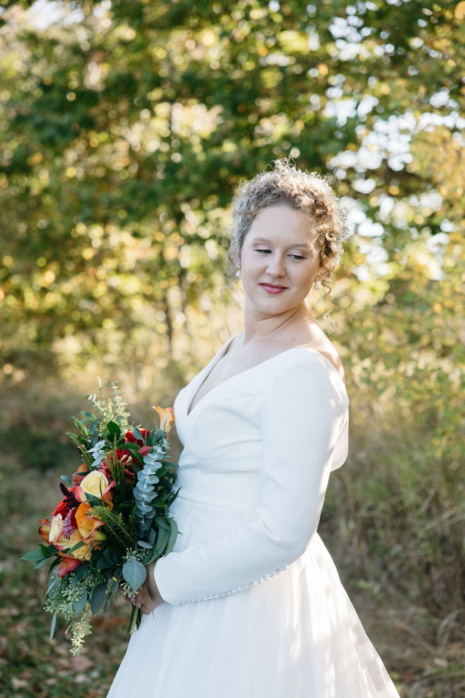 A white wedding dress glows in golden autumn sunlight among trees and fallen leaves.