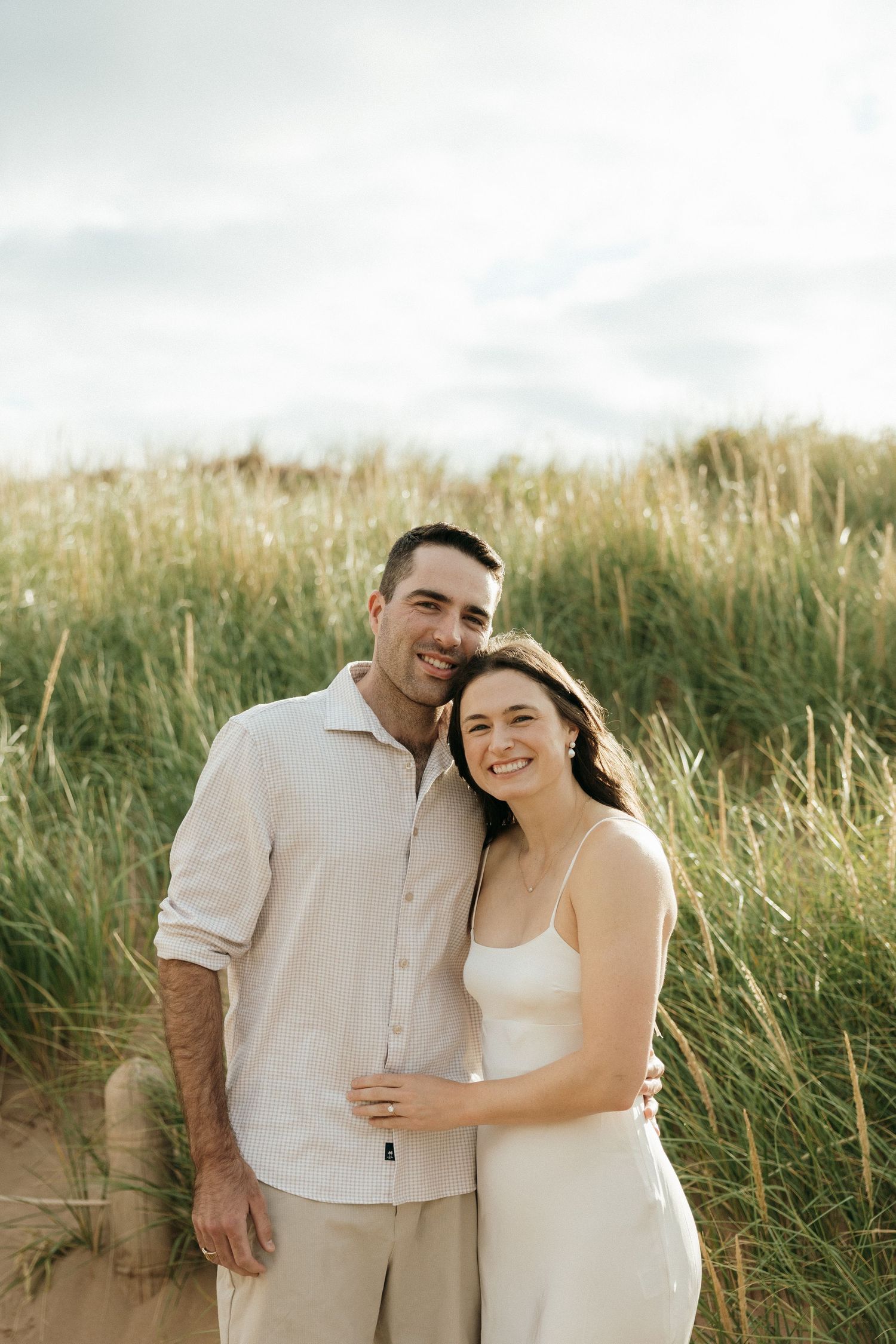 A couple in white outfits shares intimate moments while posing in a grassy field.