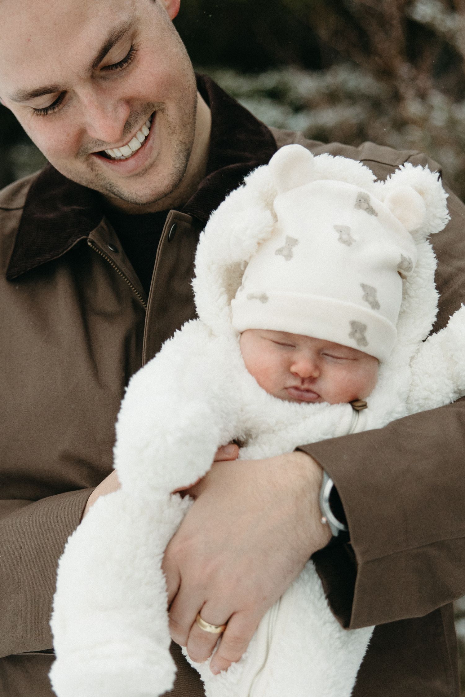 Baby bundled in soft white winter clothing being held in snowy outdoor setting.