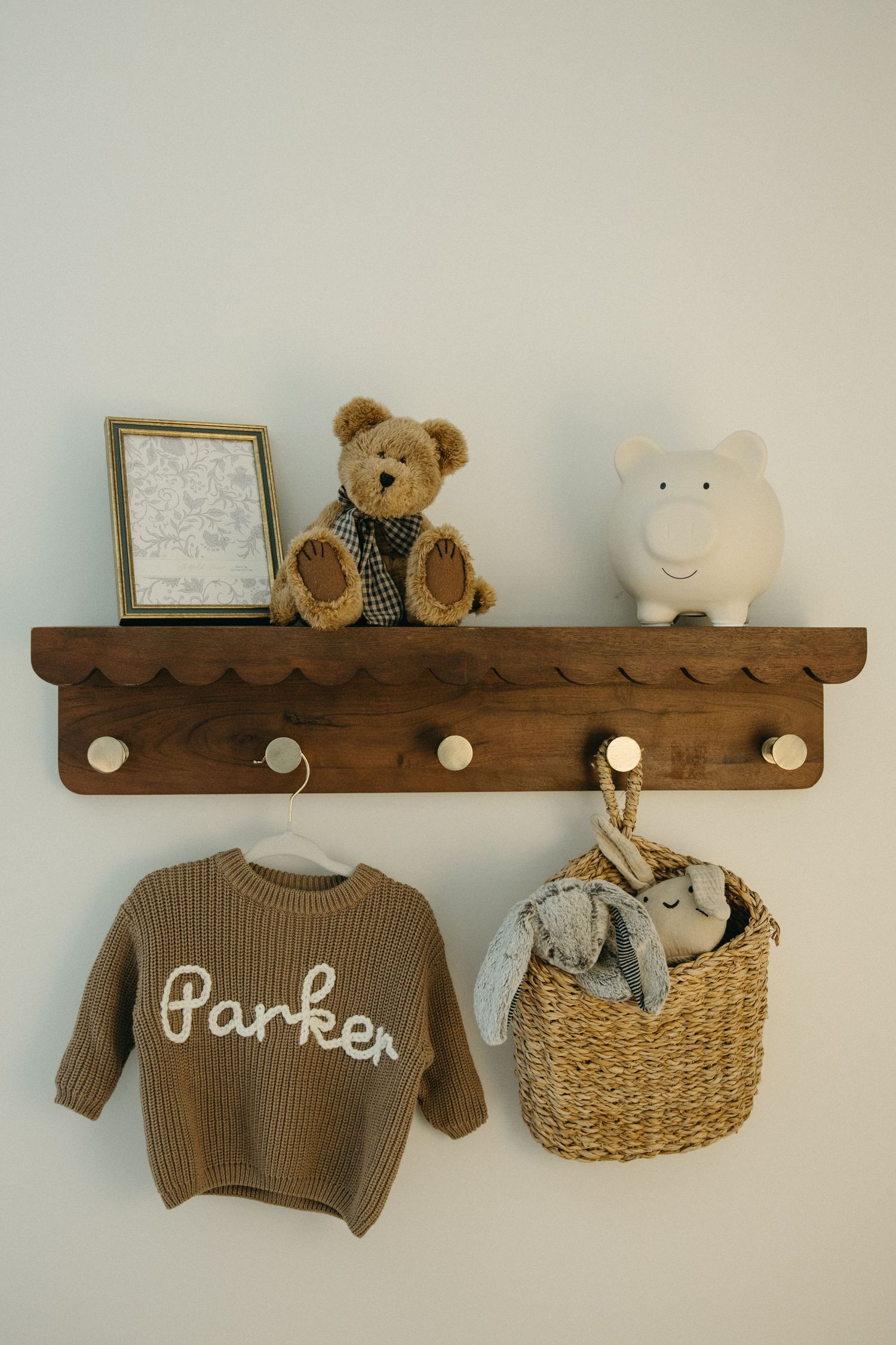 Wooden wall shelf displaying brown sweater, stuffed animals, and woven basket in nursery.