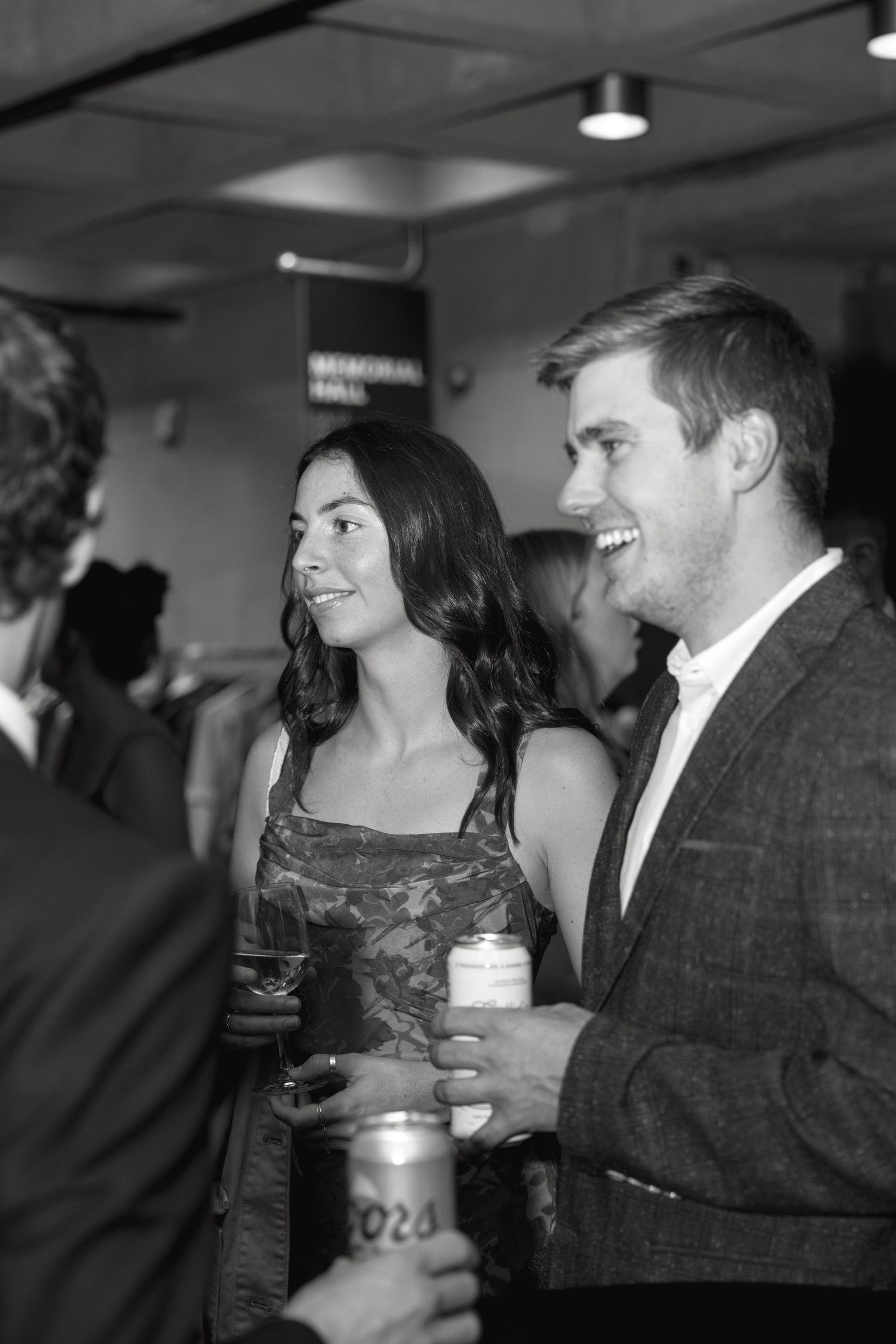 Candid black and white shot of party guests engaged in conversation while holding drinks.