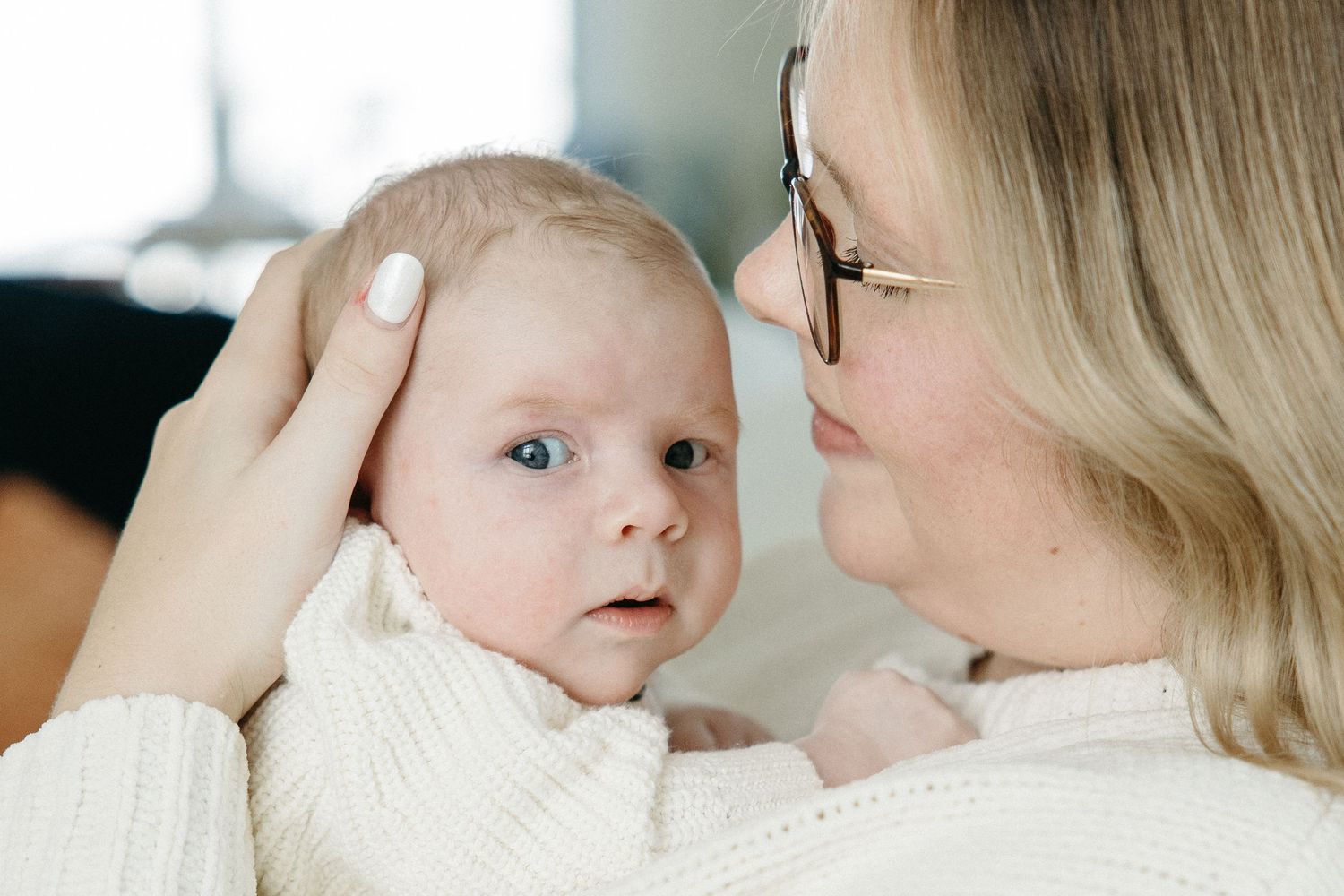 A tender moment between parent and baby in white sweaters as they share a close embrace.