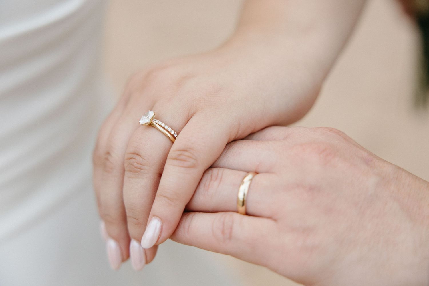 Close-up of bride and groom holding hands showing gold wedding rings.