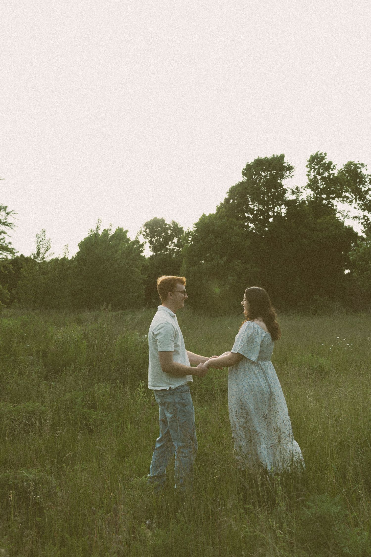 Two figures walk hand in hand through a misty field at dusk with trees silhouetted in the background.