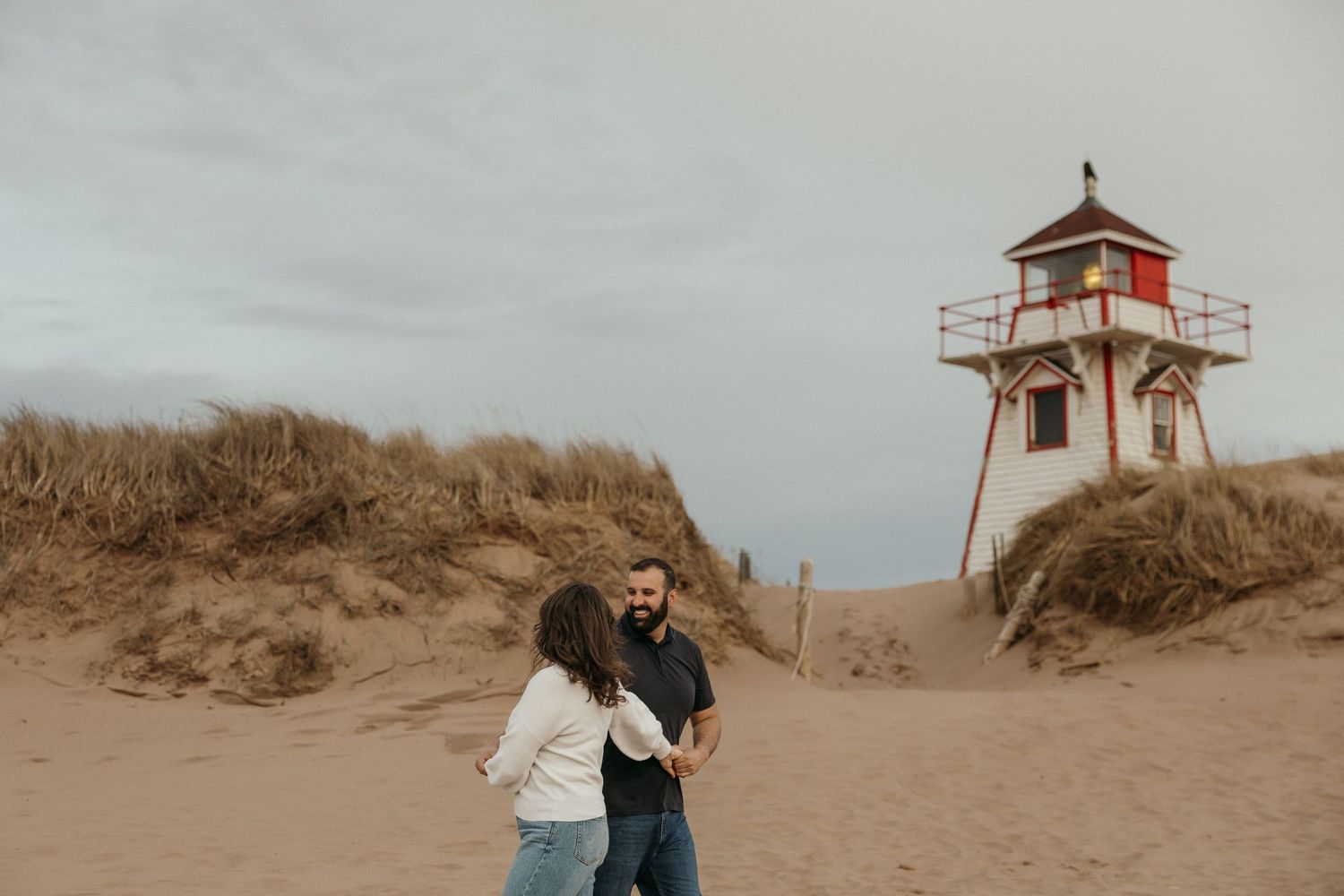 Romantic coastal engagement photos with a red and white lighthouse in the background.