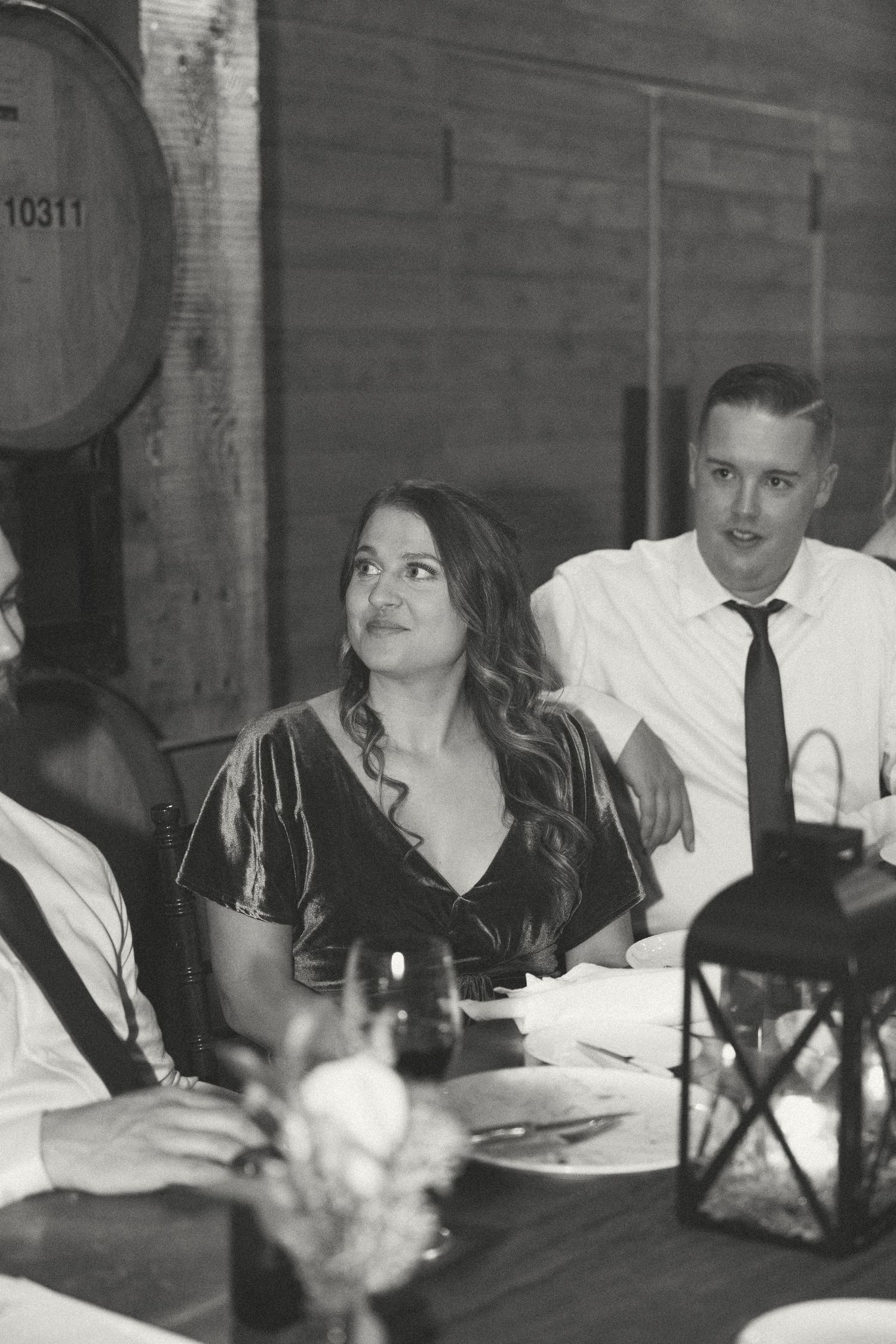 Guests seated at a dinner table in a rustic venue with wine bottles and candlelight.