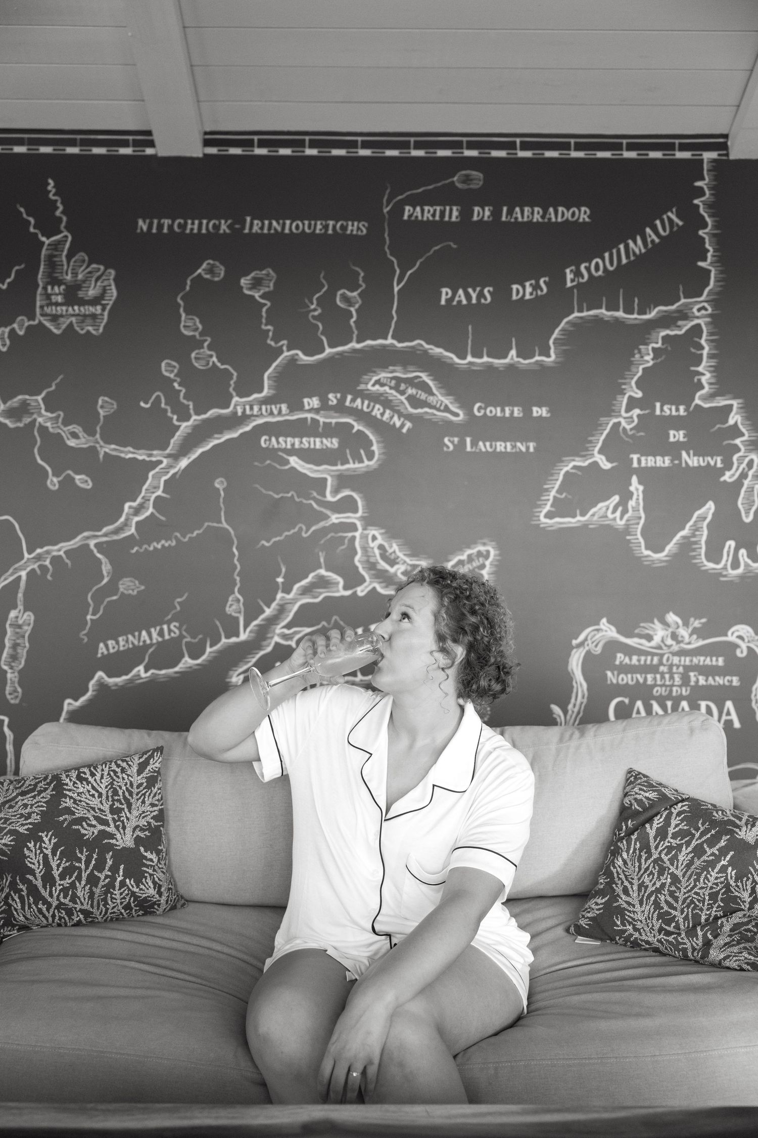 Person lounges on couch with decorative map wallpaper in black and white photograph.