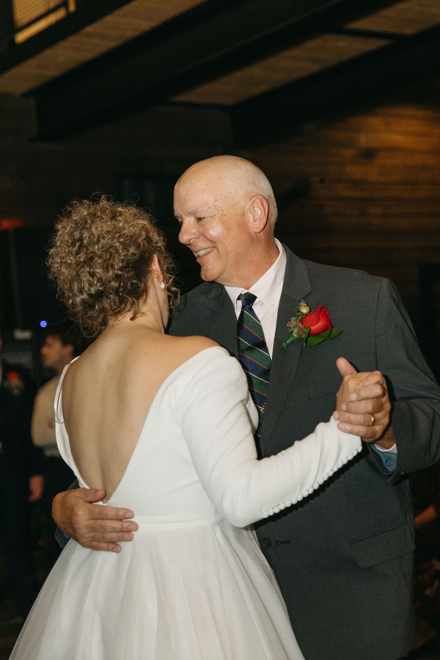 A couple shares a tender dance moment at a wedding reception in a rustic venue.