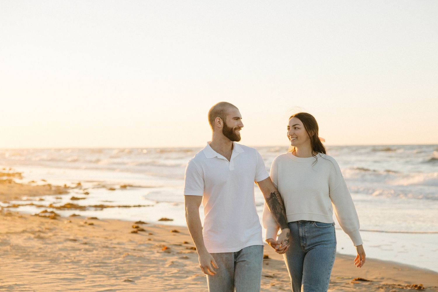 Couple walking hand in hand along shoreline during sunset beach session.