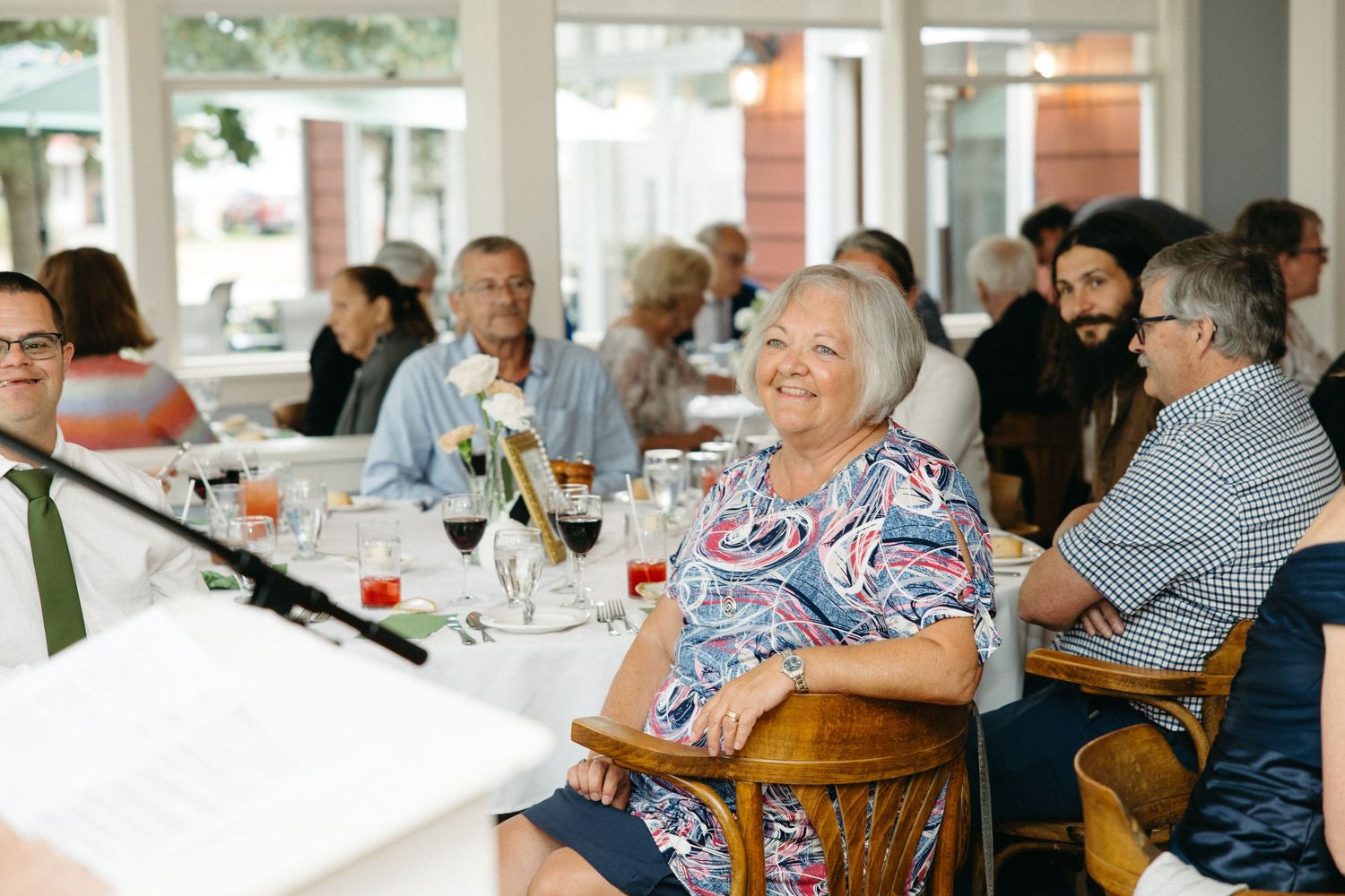Smiling woman in floral dress enjoying wedding reception dinner with guests.