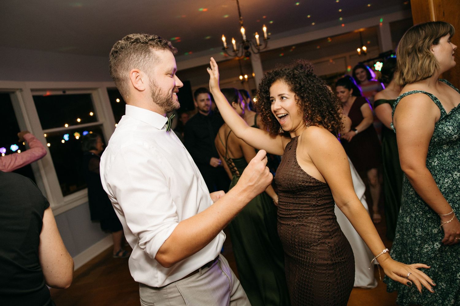 A man and woman dance and laugh together energetically at a lively wedding reception.