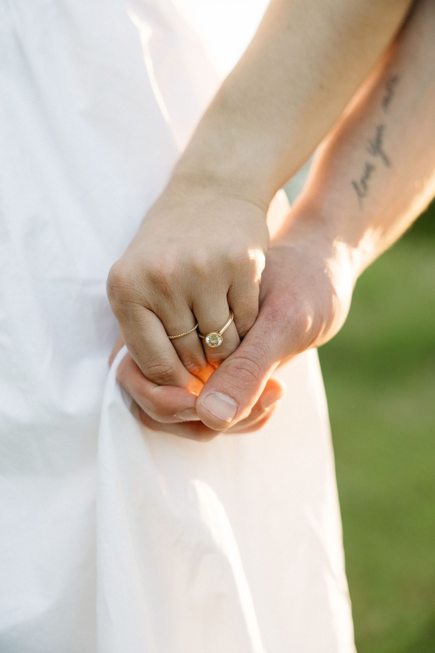 Close-up of couple holding hands, woman wearing diamond engagement ring, man with love tattoo on wrist.