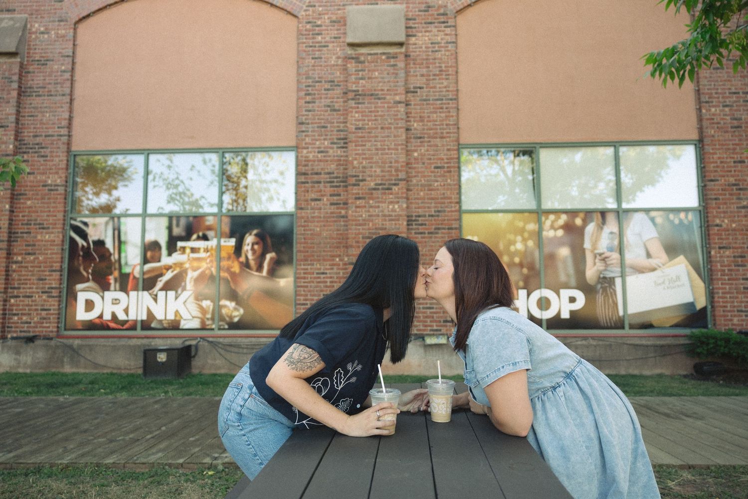 Friends sitting at an outdoor table near a brick building with shop windows.