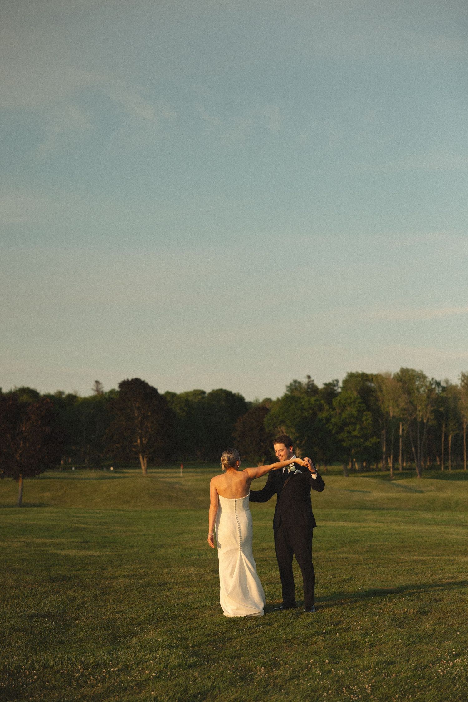 Couple dances together on a golf course during sunset.