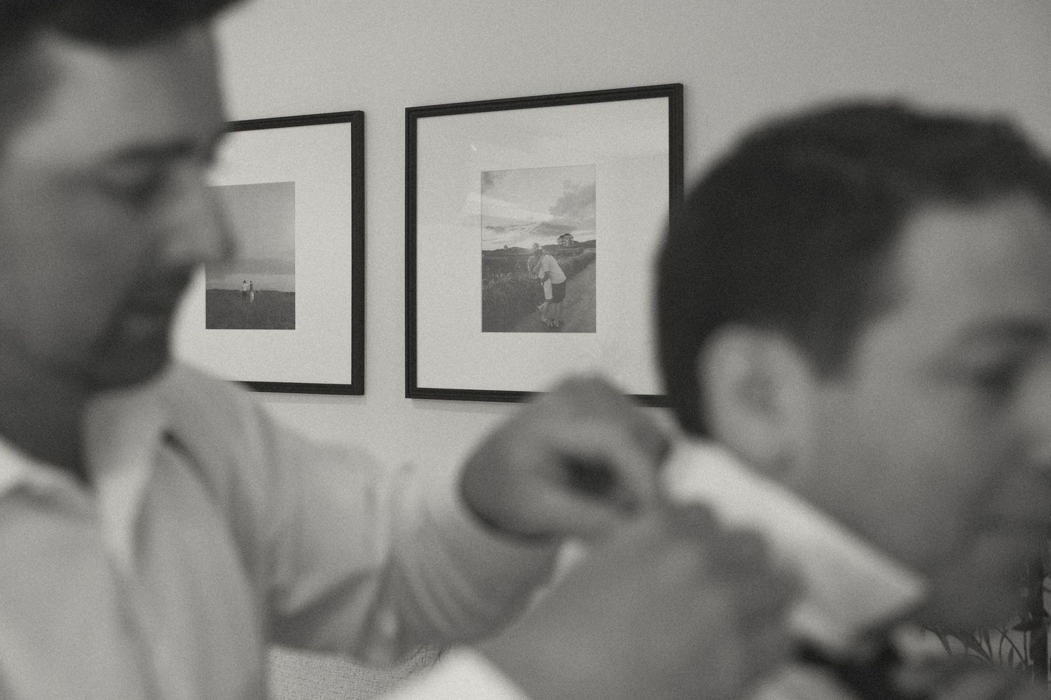 A series of black and white photos hanging on a white wall with people viewing them.