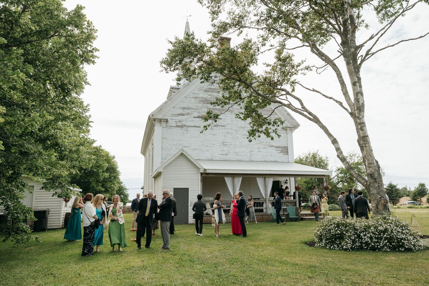 Guests gather outside a charming white country church for a wedding celebration.