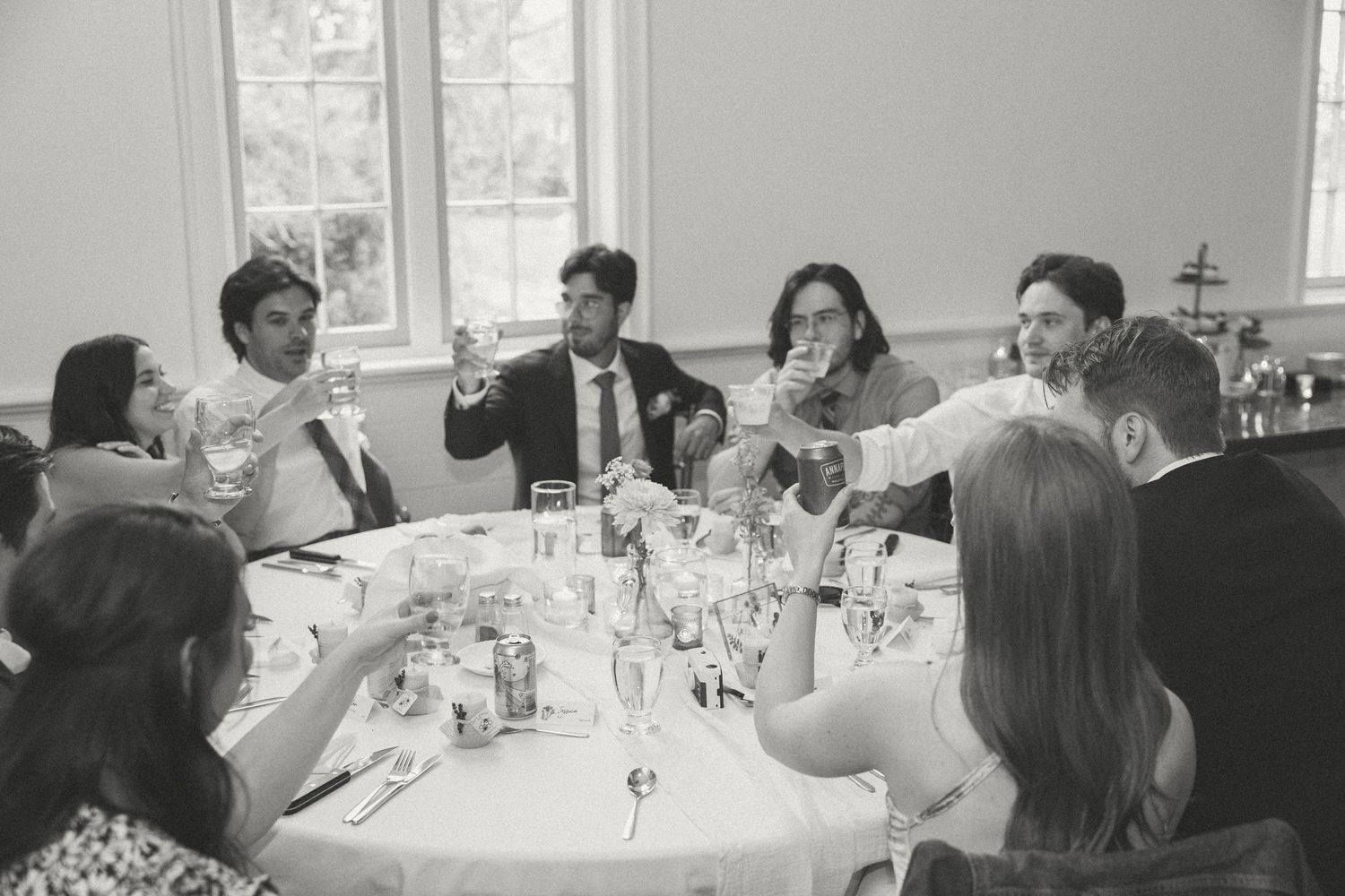 Black and white photo of wedding reception guests enjoying speeches at round tables.