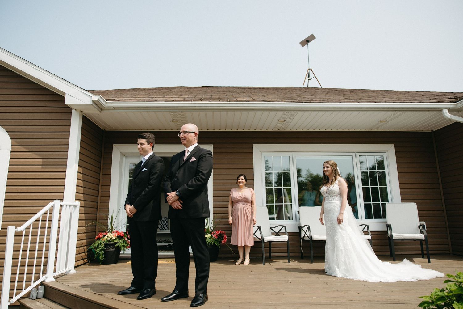 Wedding party poses for photos on a porch of a beige house.