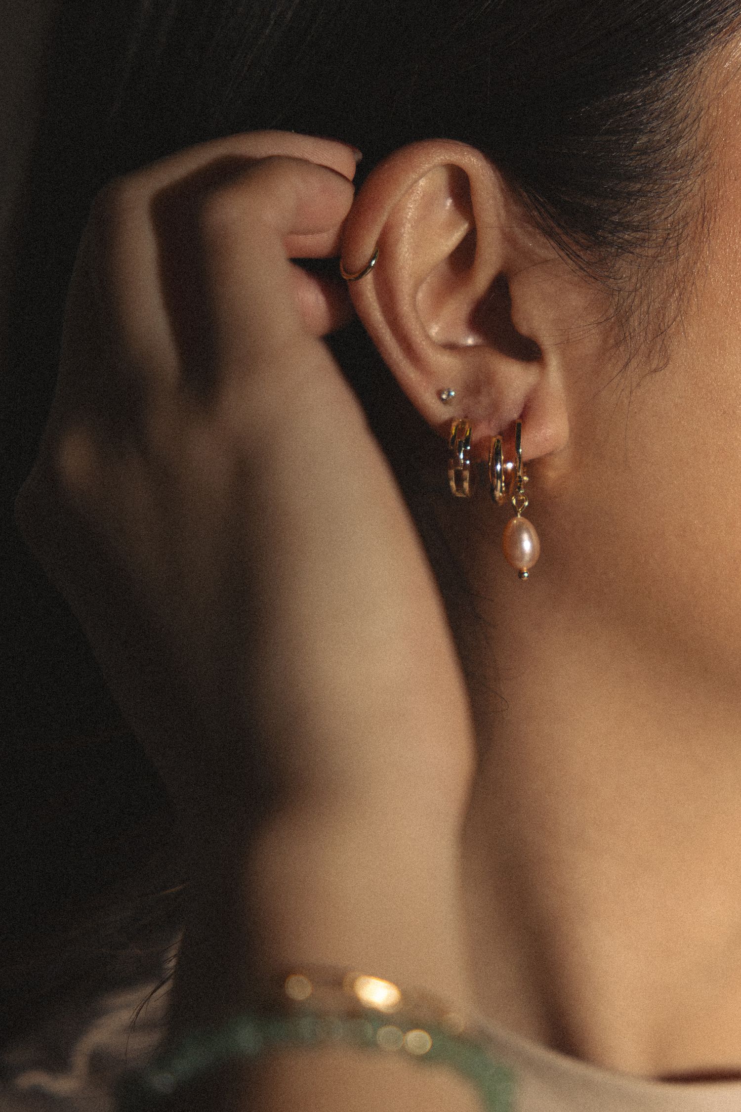 Multiple gold ear piercings and jewelry shown in dramatic side profile.