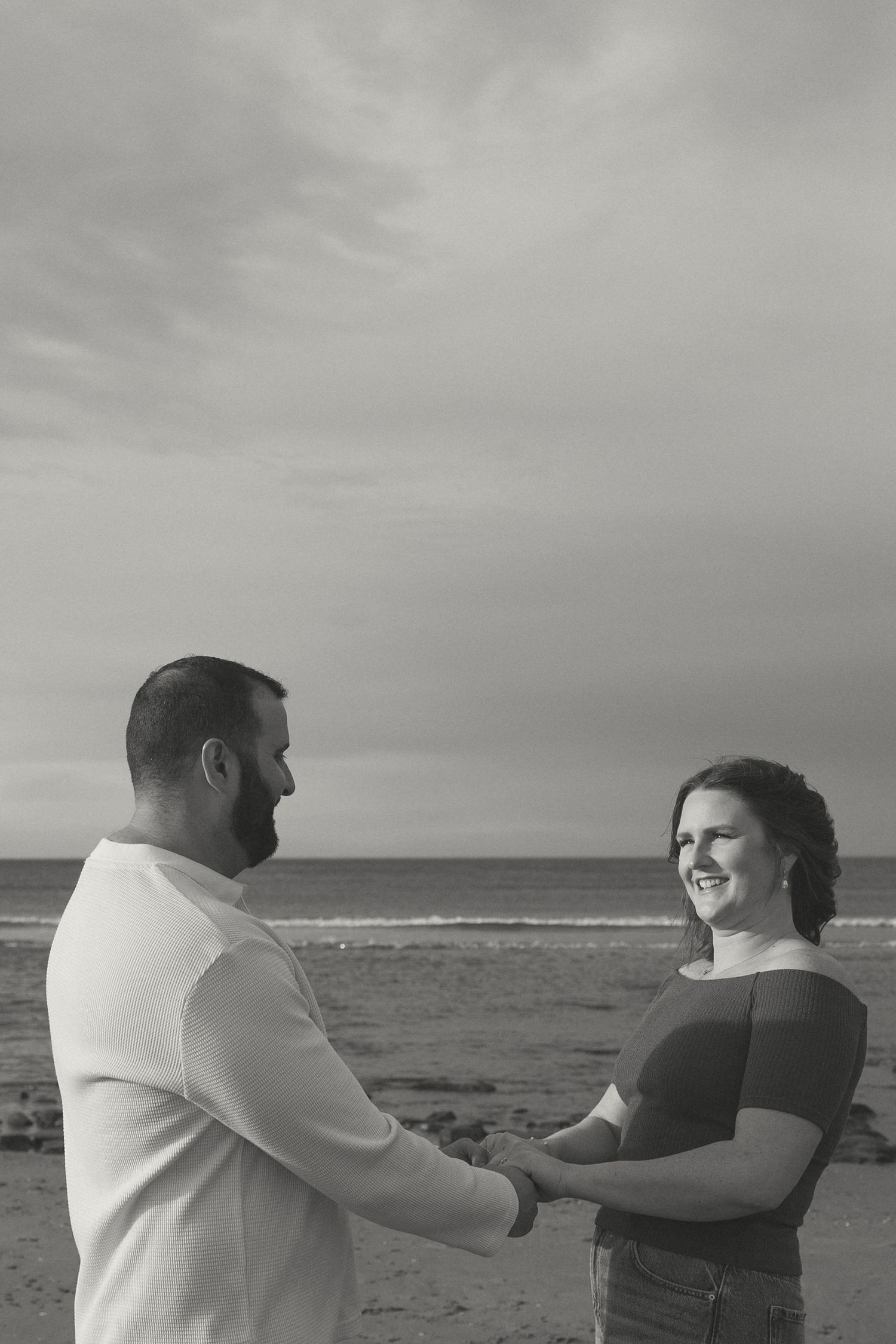 A couple shares a tender moment together on a cloudy beach with the ocean in the background.