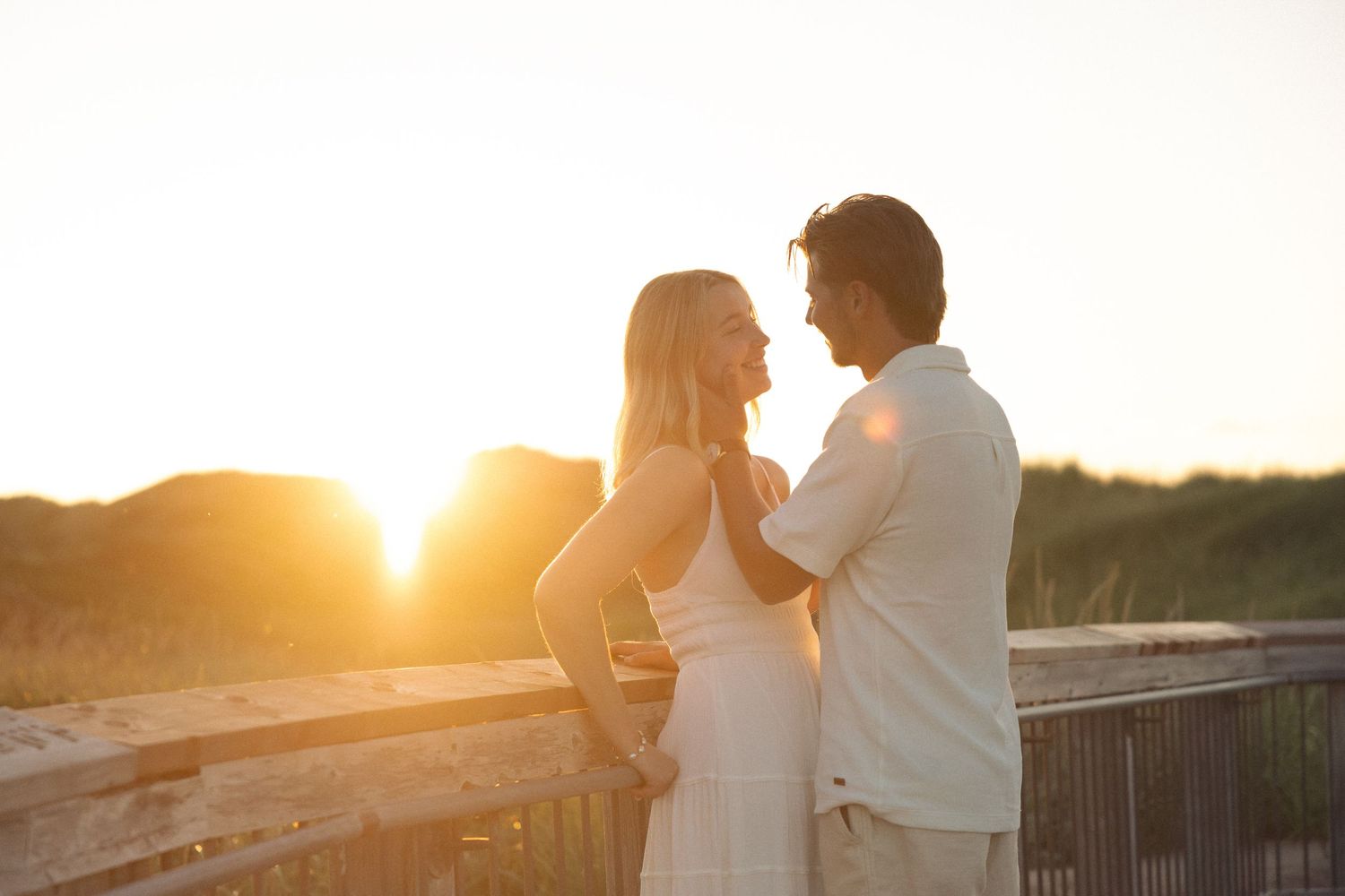 Couple embracing on a beach boardwalk at golden sunset, romantic outdoor portrait with warm glowing backlight.