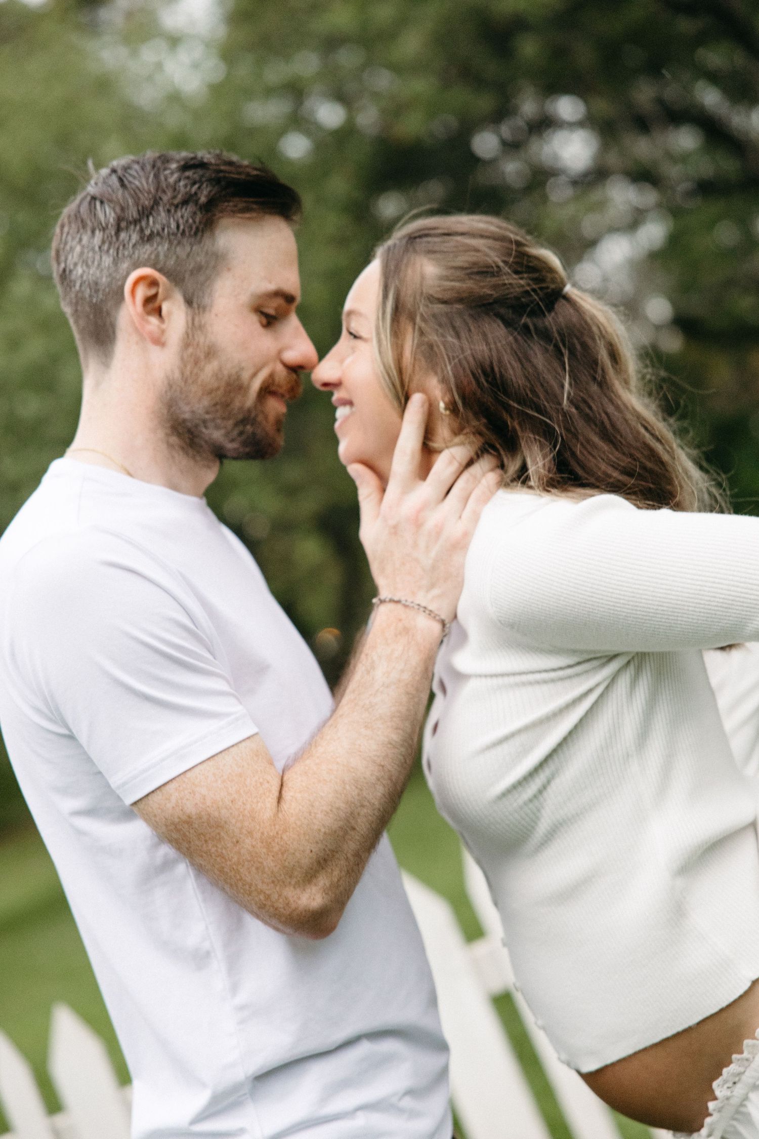 A loving couple shares a tender moment, nearly kissing outdoors in a lush green garden setting.
