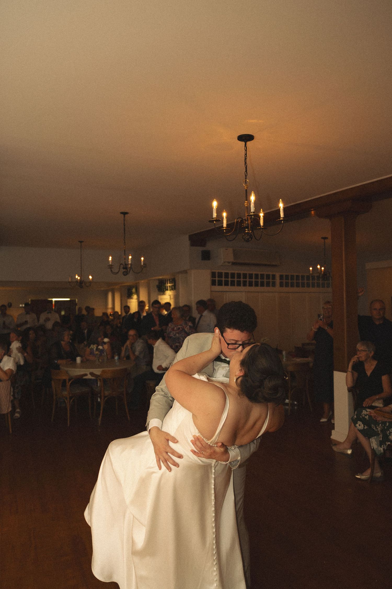 Bride and groom share romantic first dance kiss in warmly lit wedding venue.