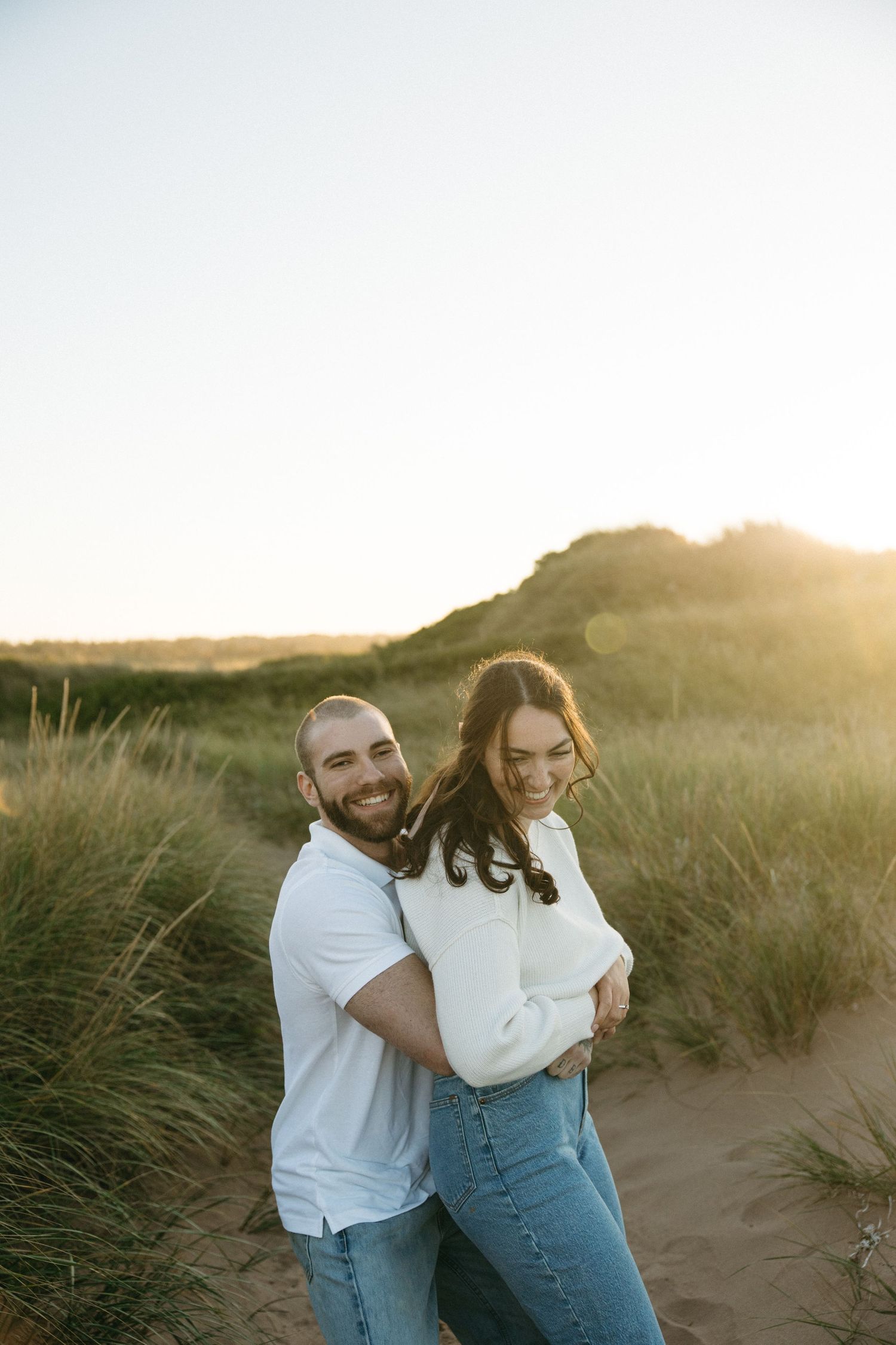 Joyful couple laughing together in beach grass during golden hour.